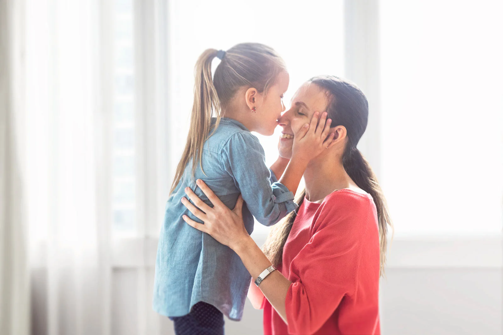 Mother and daughter embracing at home in front of a back lit window
