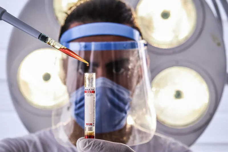 A lab worker wearing a face shield filling a vial with a dropper